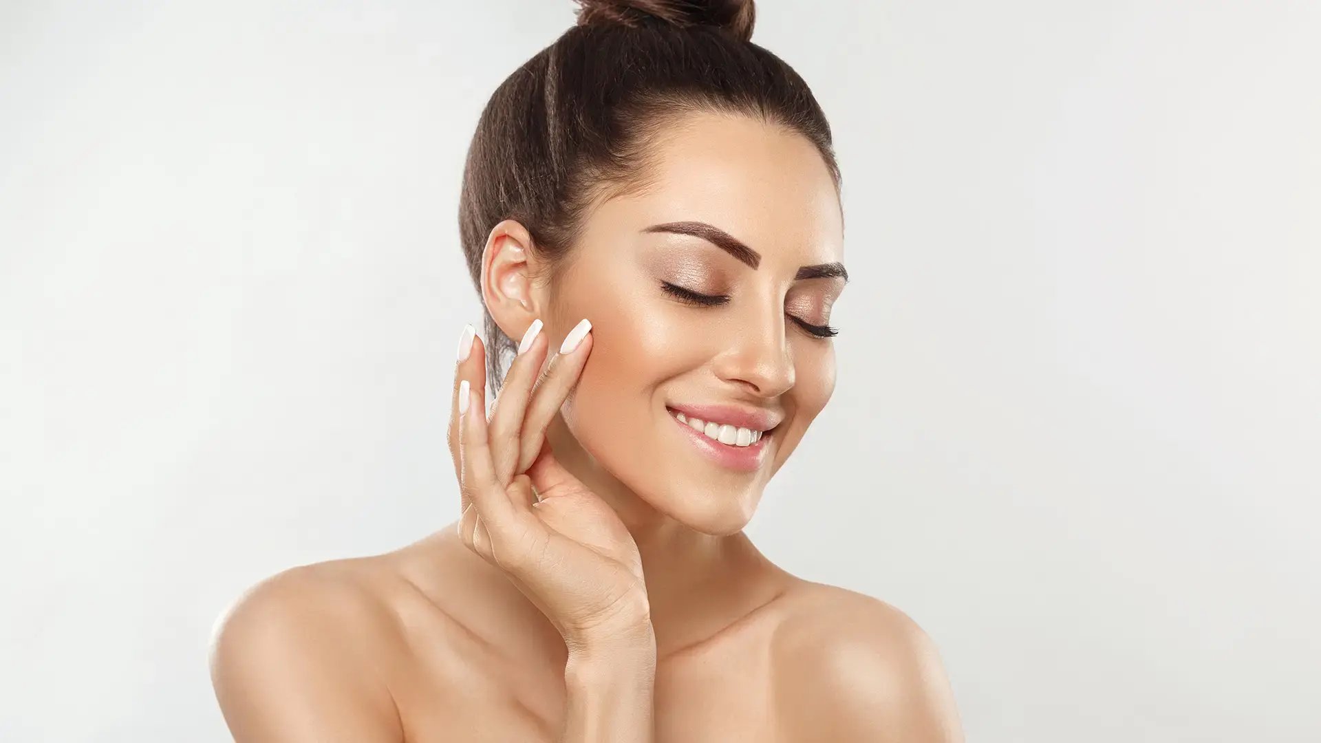 Beautiful young woman with clean perfect skin. Portrait of beauty model with natural nude make up and touching her face. Spa, skincare and wellness_